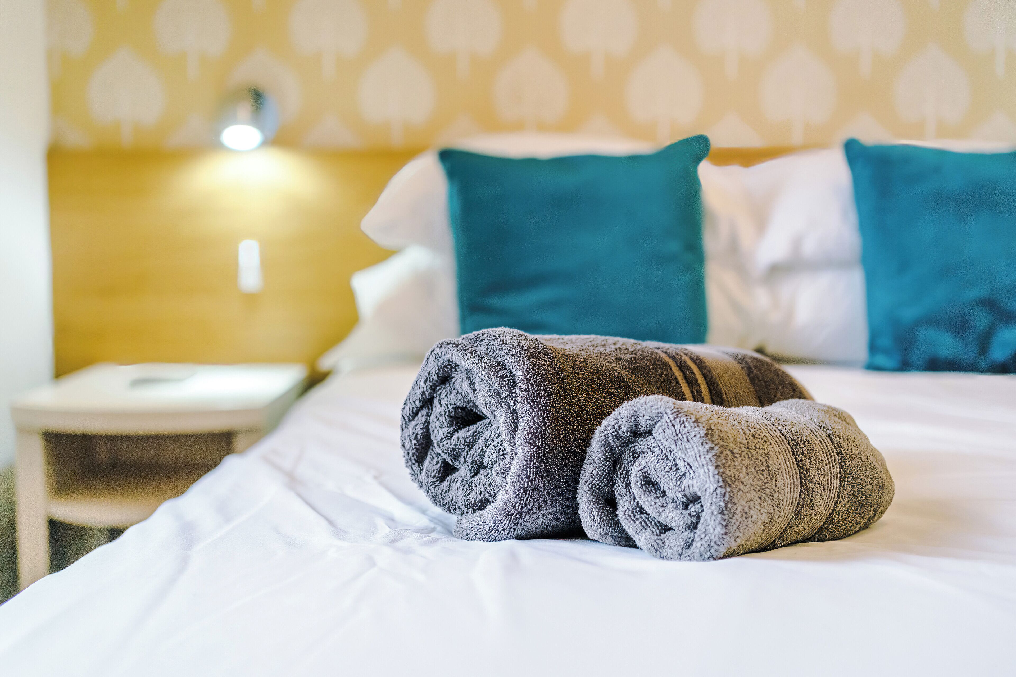 Un lit bien fait, avec des serviettes pliées et des coussins de couleur turquoise.