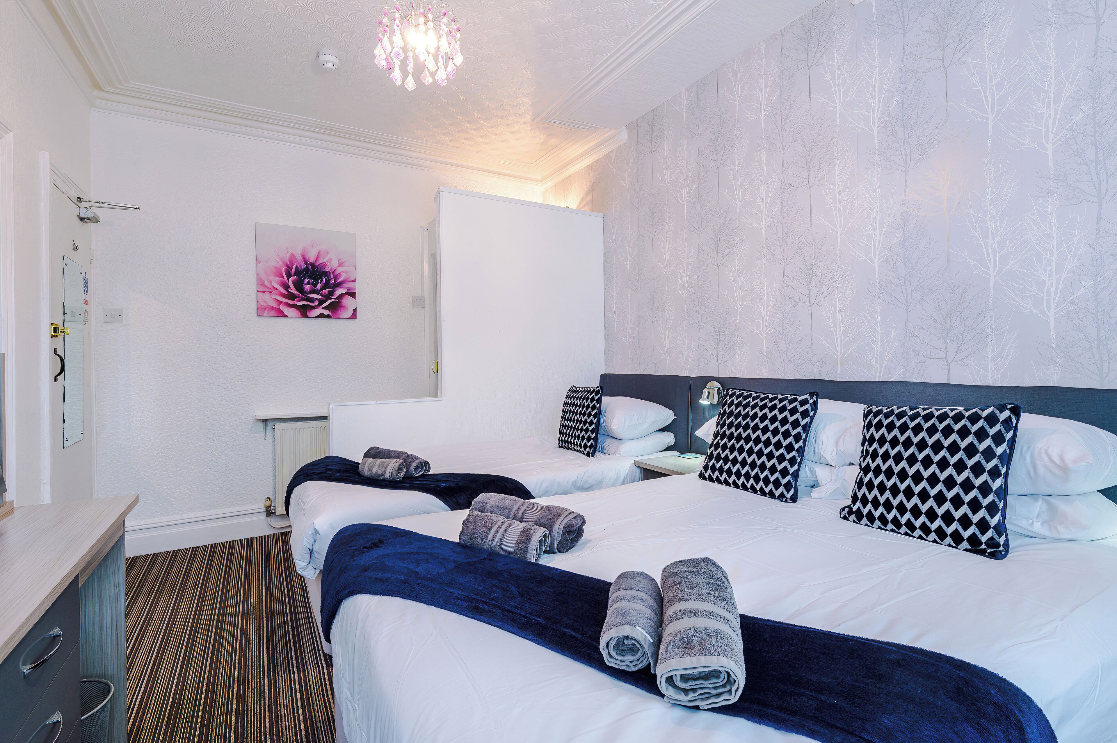 Habitación de hotel con dos camas, un ventanal grande, un radiador y una obra de arte colgada en la pared.