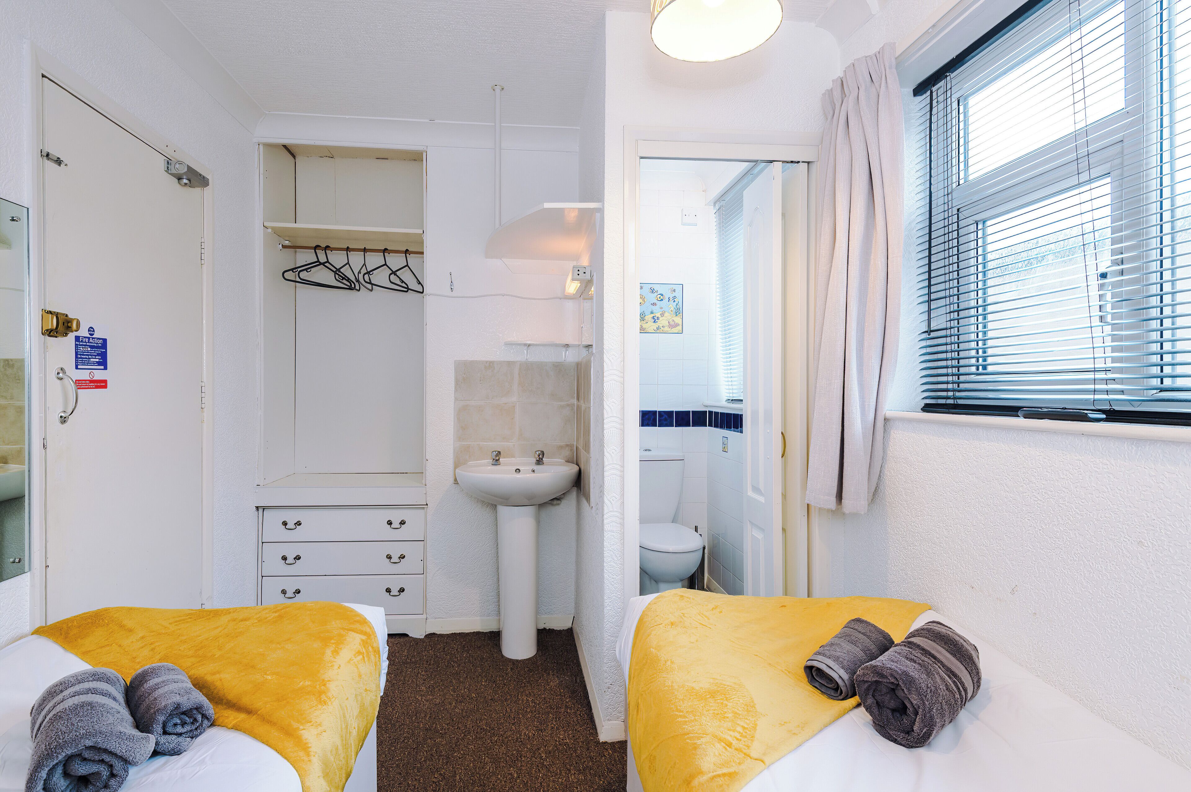 Une chambre d’hôtel avec deux lits, une salle de bain et une fenêtre avec des stores.