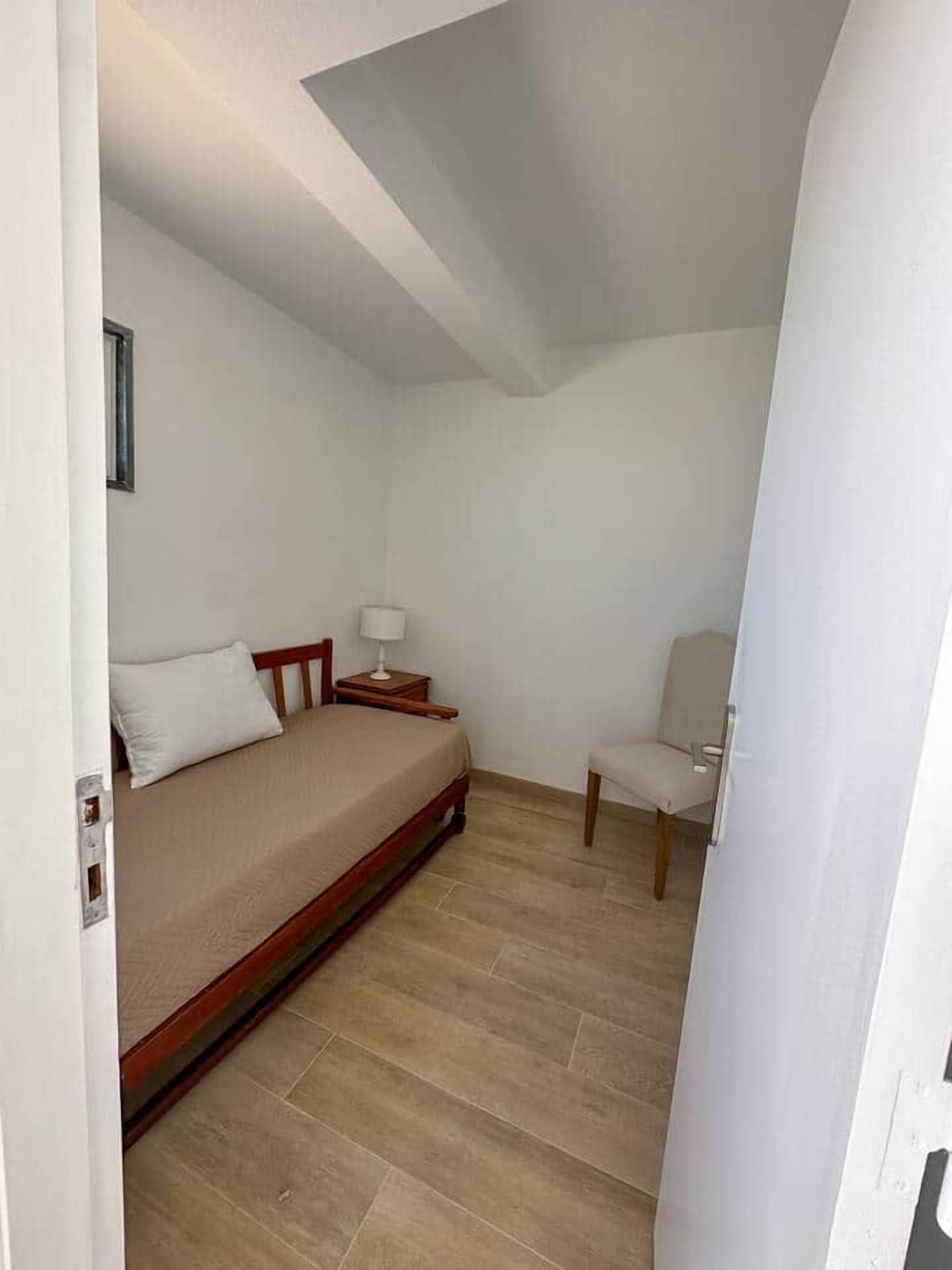 Een kleine, eenvoudig gemeubileerde kamer met een bed, een stoel en een nachtkastje.