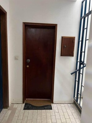 A wooden door with a doorknob, a small wooden cabinet, and a black doormat with "WELCOME" on it.