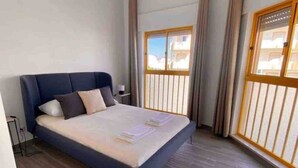 A modern hotel room with a large bed, a bedside table, and a window with a view of buildings. - Minimalist Nomad Seaside Apartment (Quarteira)