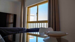 A hotel room with a large window, a flat-screen TV mounted on the wall, a table with a plate and a cup, and a chair. - Minimalist Nomad Seaside Apartment (Quarteira)