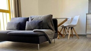 A modern living room with a grey sofa, a dining table with white chairs, and a wooden floor. - Minimalist Nomad Seaside Apartment (Quarteira)
