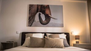 A bedroom with a large bed, multiple pillows, a headboard, bedside tables, and a wall-mounted elephant artwork. - Seaside Inspire Wilderness (Quarteira)