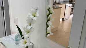 A white orchid in a clear vase on a white console table, with a mirror reflecting a kitchen area. - Rooftop Sea View Apartment (Quarteira)