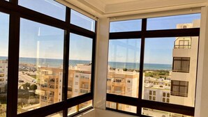 A room with large windows offering a view of a coastal cityscape. - Rooftop Sea View Apartment (Quarteira)