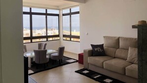 A modern living room with a sofa, a coffee table, and chairs. Large windows offer a view of the cityscape. - Rooftop Sea View Apartment (Quarteira)