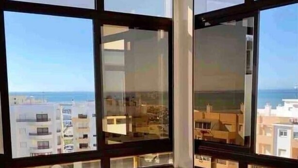 A modern room with a glass table, two chairs, and a view of the city and sea. - Rooftop Sea View Apartment (Quarteira)