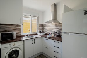 Uma cozinha compacta com máquina de lavar, micro-ondas, pia e um exaustor em aço inoxidável.