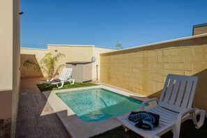 Piscina com duas cadeiras de descanso brancas, uma com toalha e um par de sapatos.