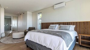 Un dormitorio moderno con una cama grande, cabecera de madera, mesita de noche y un banco empotrado.