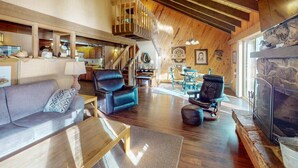 A spacious living area with a fireplace, leather chairs, a sofa, and a staircase leading to an upper level.