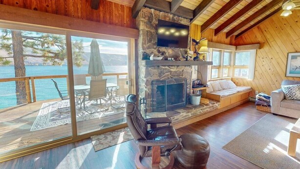 A cozy cabin with a stone fireplace, wooden beams, a balcony with a view of the water, and a comfortable seating area.