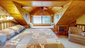 A cozy attic bedroom with a large bed, a chair, and a window overlooking a snowy landscape. - The Treehouse lakefront– scenic family getaway (Joseph)