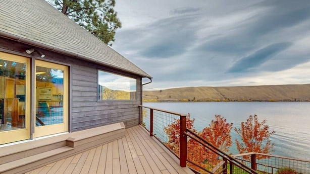 A wooden deck with a glass door, a small window, and a view of a lake with hills in the background. - The Treehouse lakefront– scenic family getaway (Joseph)