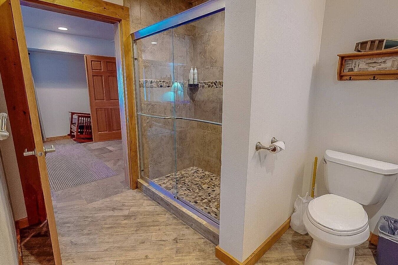A bathroom with a glass shower enclosure, a toilet, and a wooden door leading to another room.