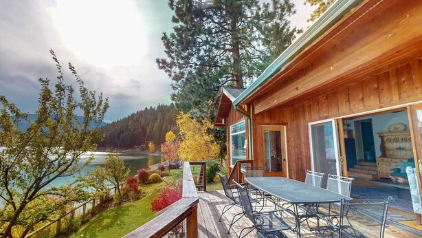 Une cabane en bois dotée d’une terrasse, d’une table avec des chaises et offrant une vue sur un lac et une forêt.