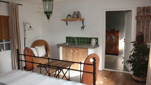 Une chambre à coucher comprenant un lit, une chaise en bois, un petit coin cuisine et une porte donnant sur une autre pièce.