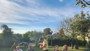 Un groupe de personnes s’est rassemblé autour d’un feu de camp, avec un réchaud posé sur un trépied. Ils étaient assis à une table de pique-nique, une bouteille et des verres à portée de main.