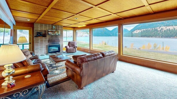 A spacious living room with a fireplace, leather sofas, a coffee table, and large windows offering a view of a lake and mountains. - The View: stunning Wallowa Lake views! (Joseph)