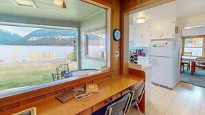 A kitchen with a view of a lake and mountains, wooden cabinets, a refrigerator, and a dining area with chairs. - The View: stunning Wallowa Lake views! (Joseph)