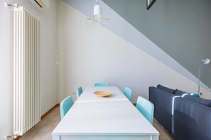 A modern dining area with a white table, light blue chairs, a wooden bowl, a dark sofa, and a white radiator. - Oasis Flat near San Gregorio Armeno (Naples)