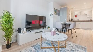 Un salon moderne doté d’un téléviseur à écran plat, d’un coin repas et d’une cuisine.