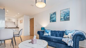 Un salon moderne avec un canapé bleu, une table basse ronde et un coin repas comprenant une table et des chaises blanches.