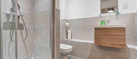 A modern bathroom with a glass shower enclosure, a toilet, and a vanity with a mirror.