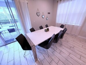 Een moderne eetkamer met een witte tafel en zwarte stoelen, een klein plantje op de tafel en een uitzicht door grote ramen.