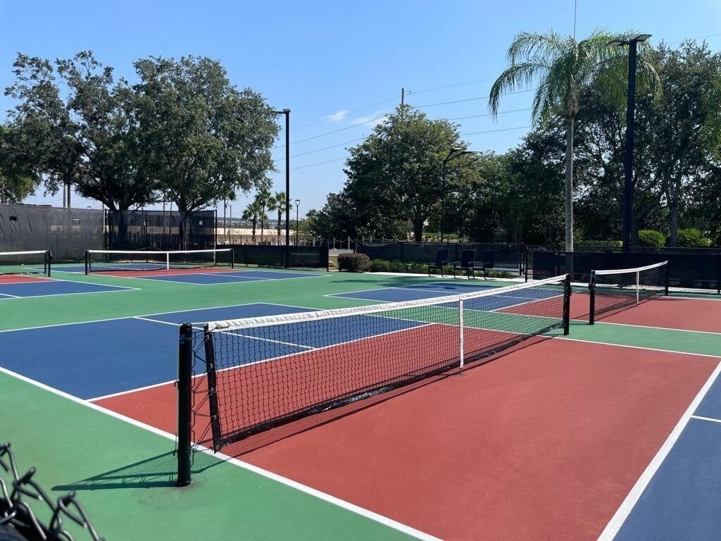 A tennis court with multiple colored surfaces and a net.