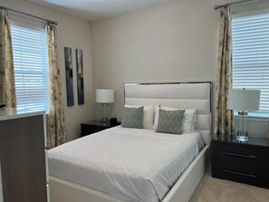 Een slaapkamer met een bed, nachtkastjes, een kaptafel en gordijnen.