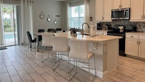A modern kitchen with white cabinetry, a central island with bar stools, a built-in microwave, and a stove. - Encore 5‑BR Home w/ Private Pool & Spa (Kissimmee)