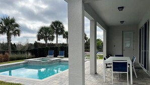 A swimming pool with a patio area, including a table and chairs, and palm trees in the background. - Encore 5‑BR Home w/ Private Pool & Spa (Kissimmee)