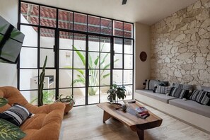 Ein Wohnzimmer mit einer Couch, einem Couchtisch und Pflanzen, mit Steinwand und großen Fenstern.