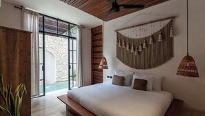 Un dormitorio con una cama grande, ventilador de techo, pared de piedra y vista a una piscina.
