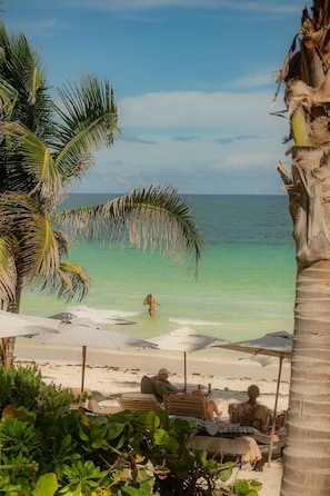 Ein Strand mit klarem türkisblauem Wasser, Palmen und Liegestühlen.
