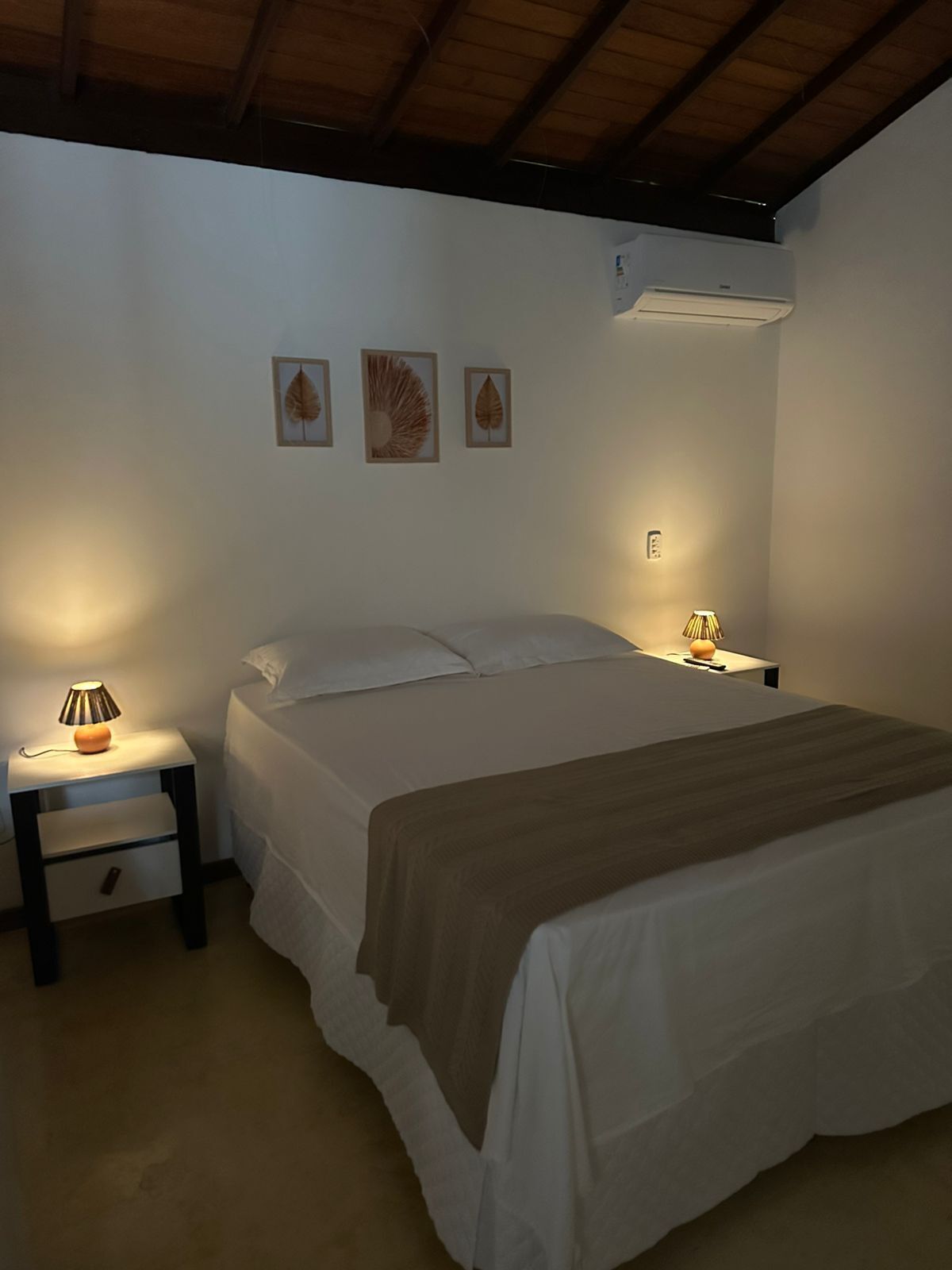 Een slaapkamer met een bed, twee nachtkastjes, een lamp en drie ingelijste kunstwerken met bladeren aan de muur.