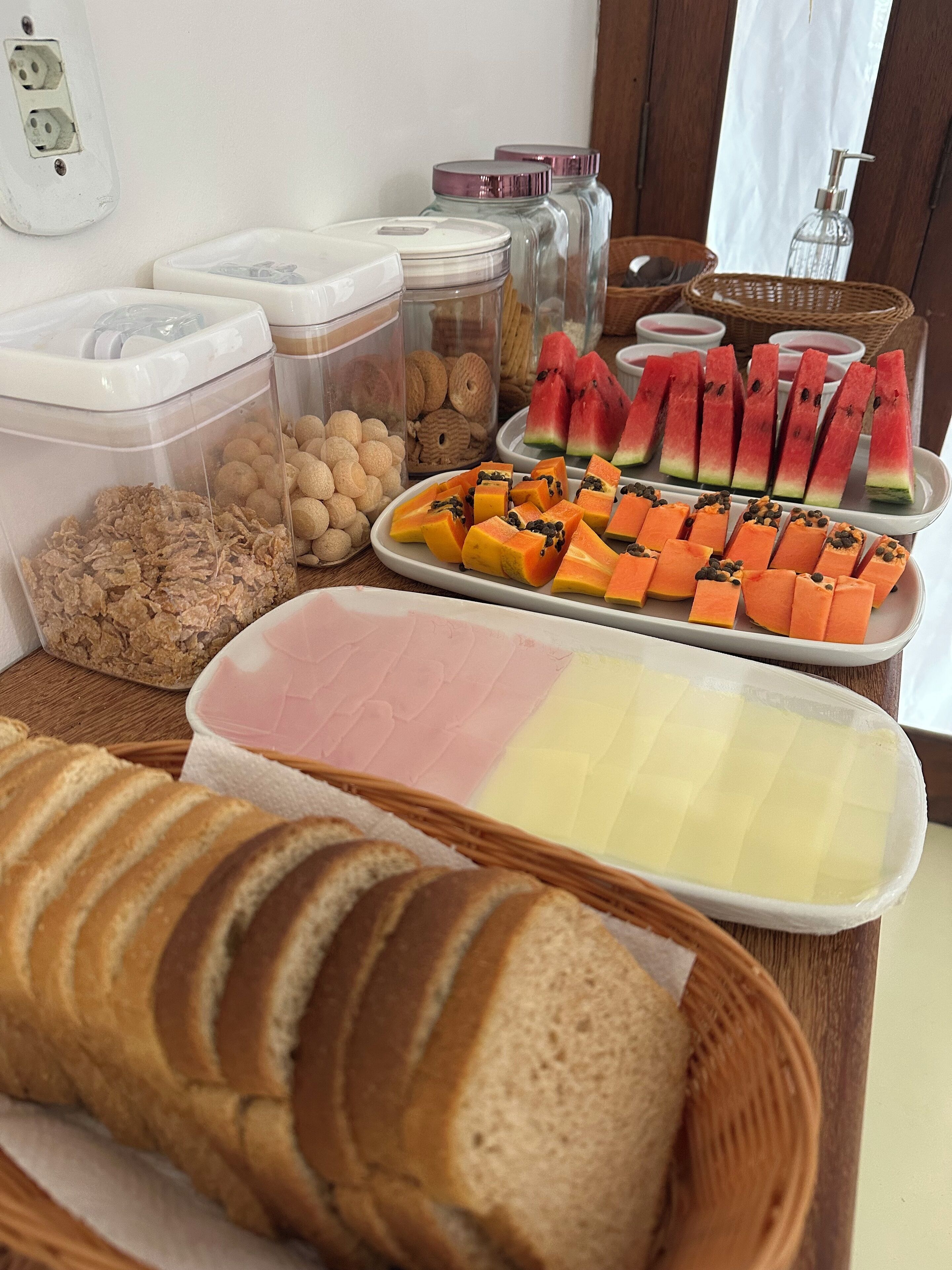 Una mesa de buffet con diversos alimentos, entre ellos sandía en rodajas, papaya y pan.