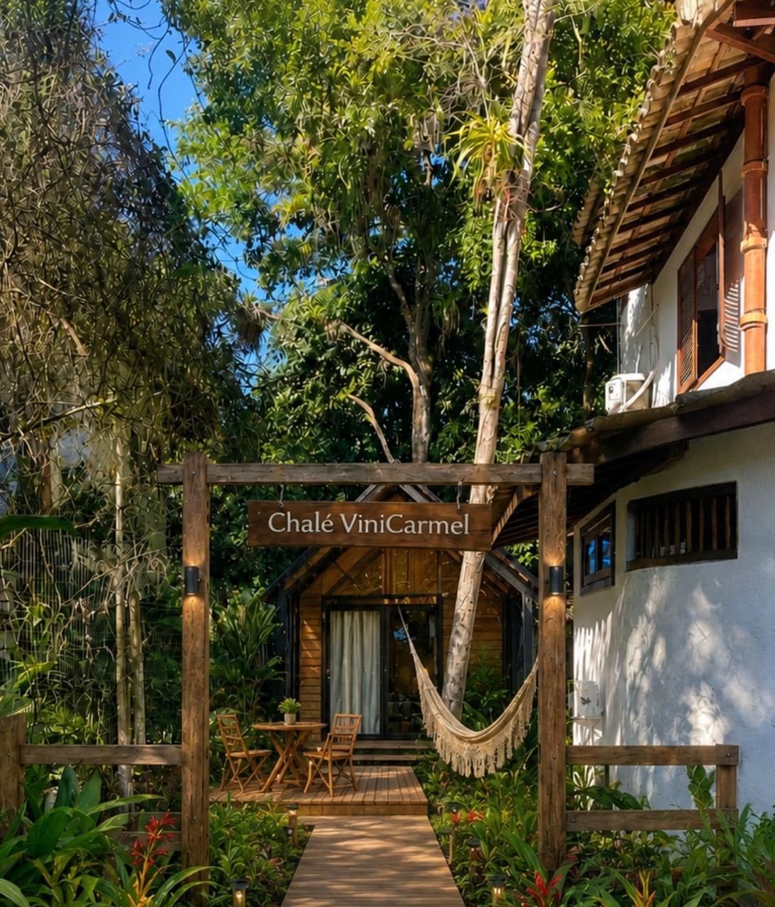 Une pergola en bois, sur laquelle on peut lire l’inscription « Chalet ViniCarmel », se trouve devant un bâtiment blanc doté d’un toit en bois.