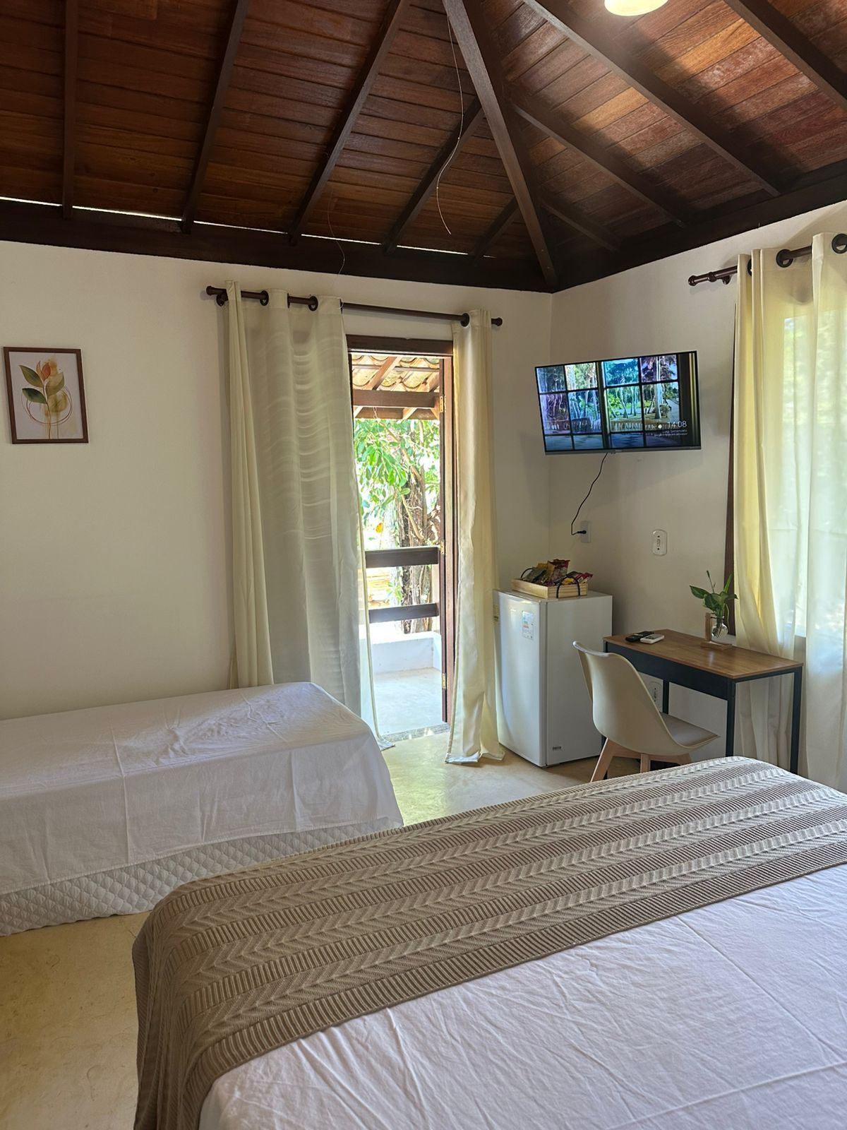 Quarto com duas camas, uma escrivaninha, televisão e um pequeno frigorífico.