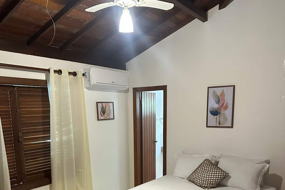 A bedroom with a bed, a ceiling fan, a window with curtains, and a door.