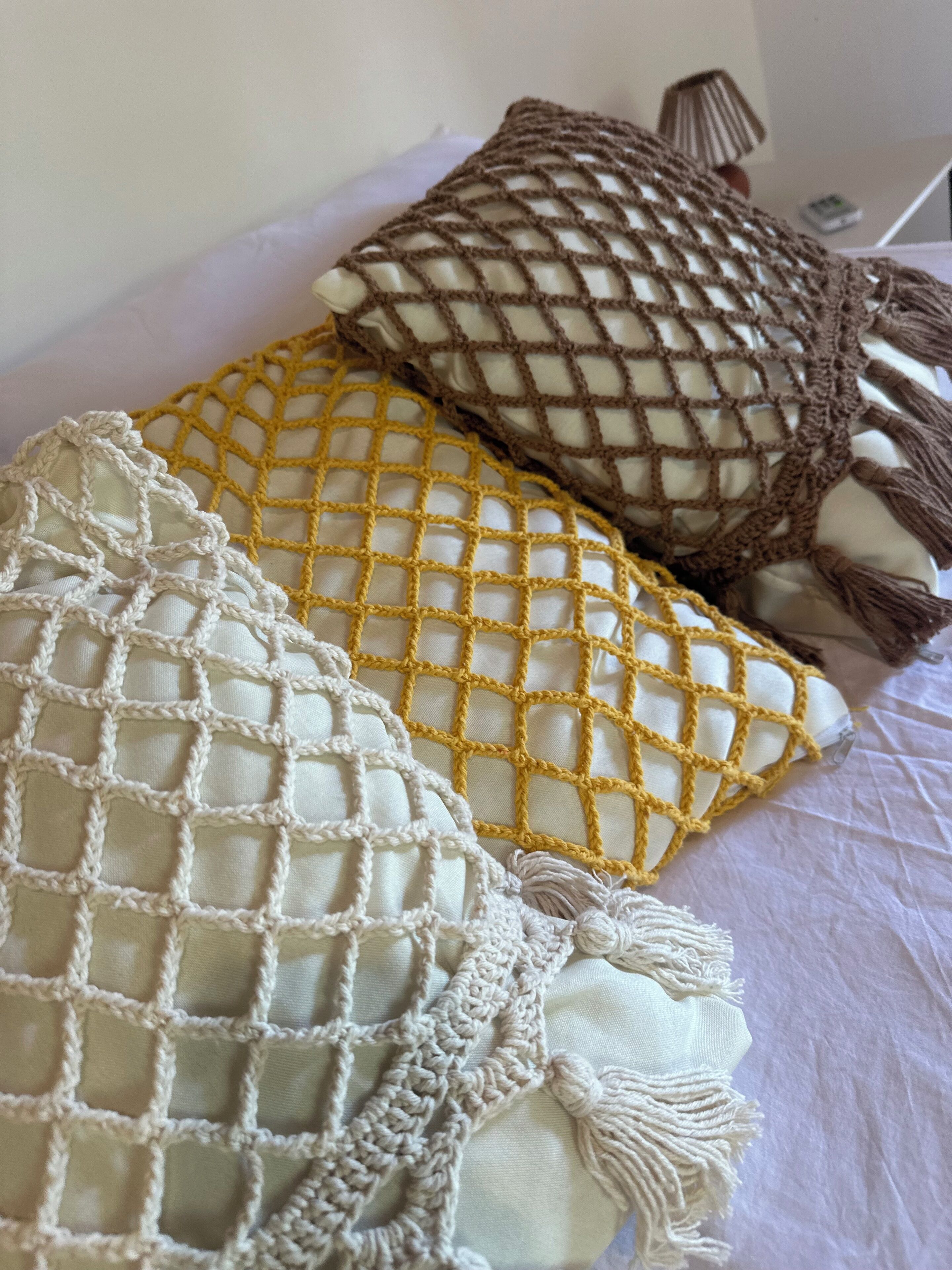 Three macramé pillows in different colors on a bed.