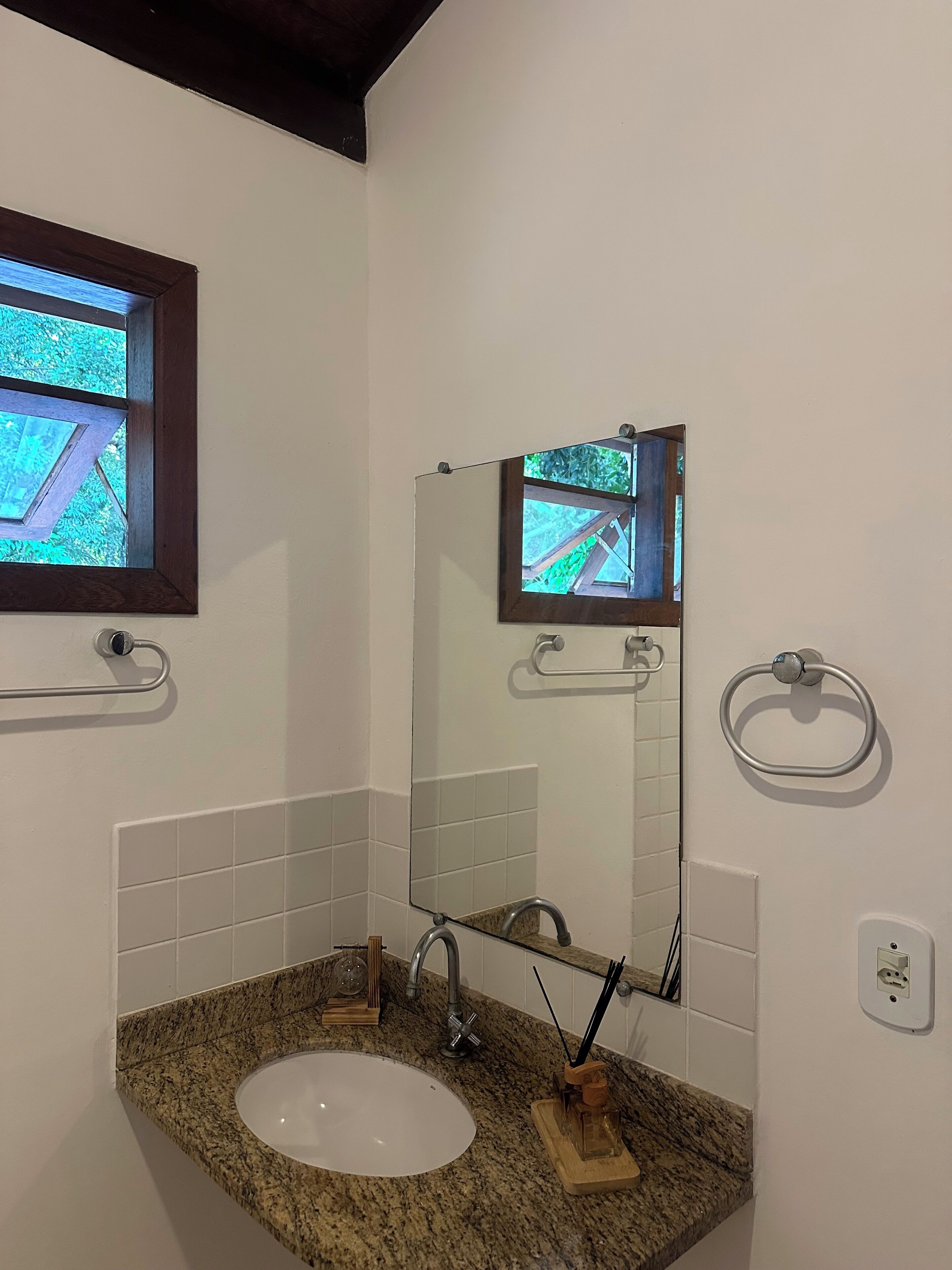 A bathroom with a granite countertop sink, a mirror, a window, and a towel ring.