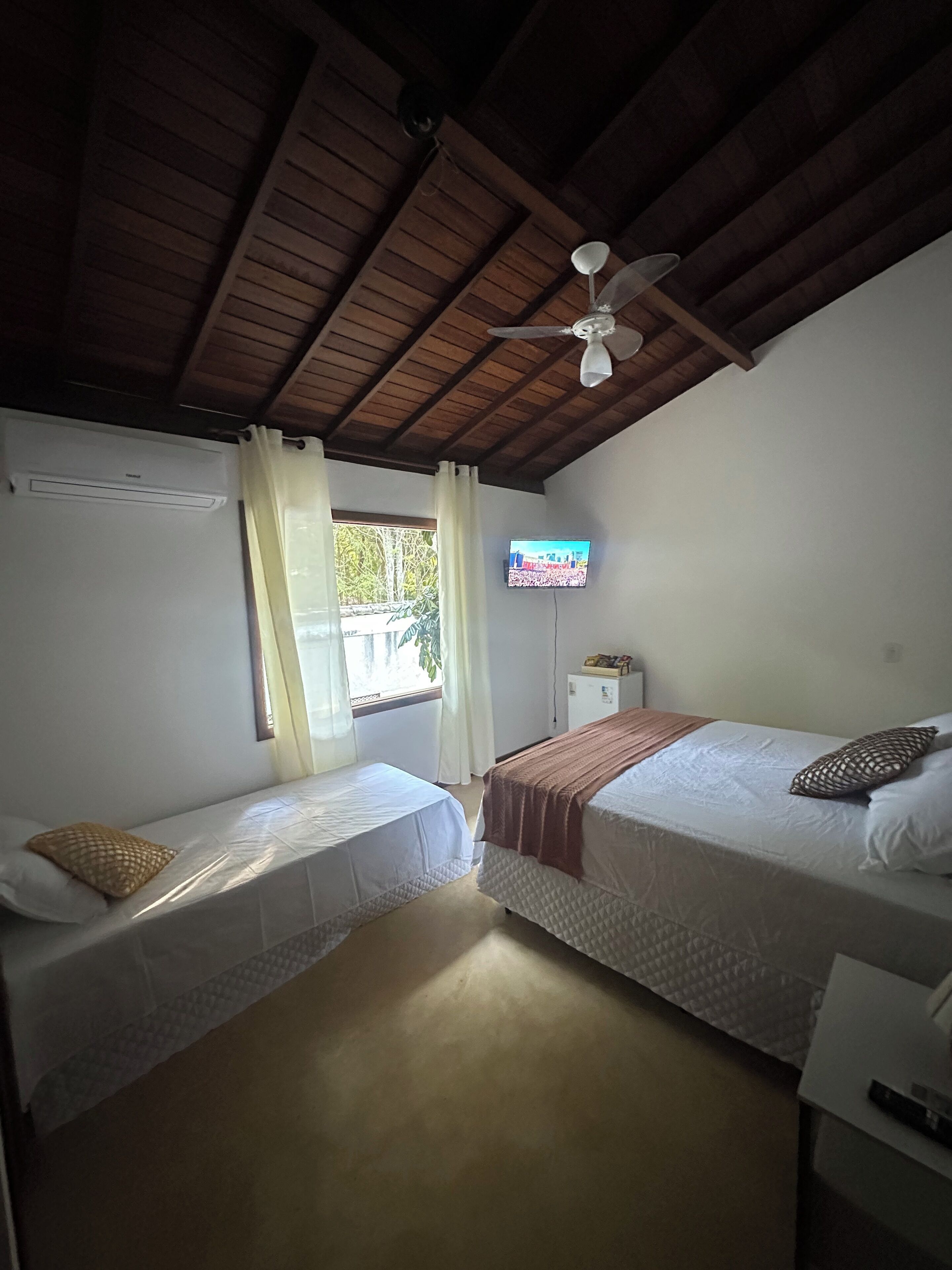 A room with two single beds, a ceiling fan, a TV, and a window with curtains.