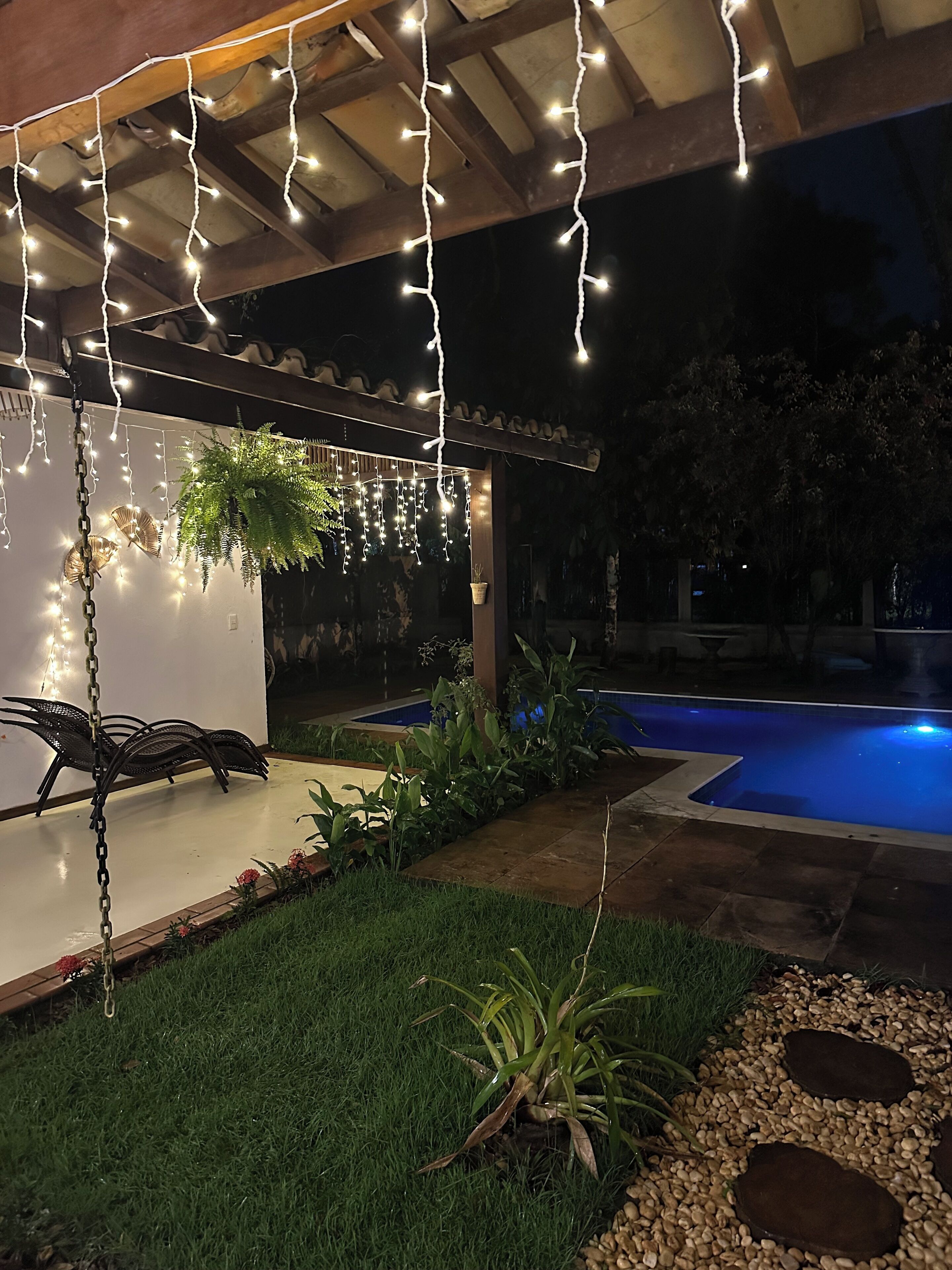 An outdoor patio area with a pool, string lights, and a swing chair.