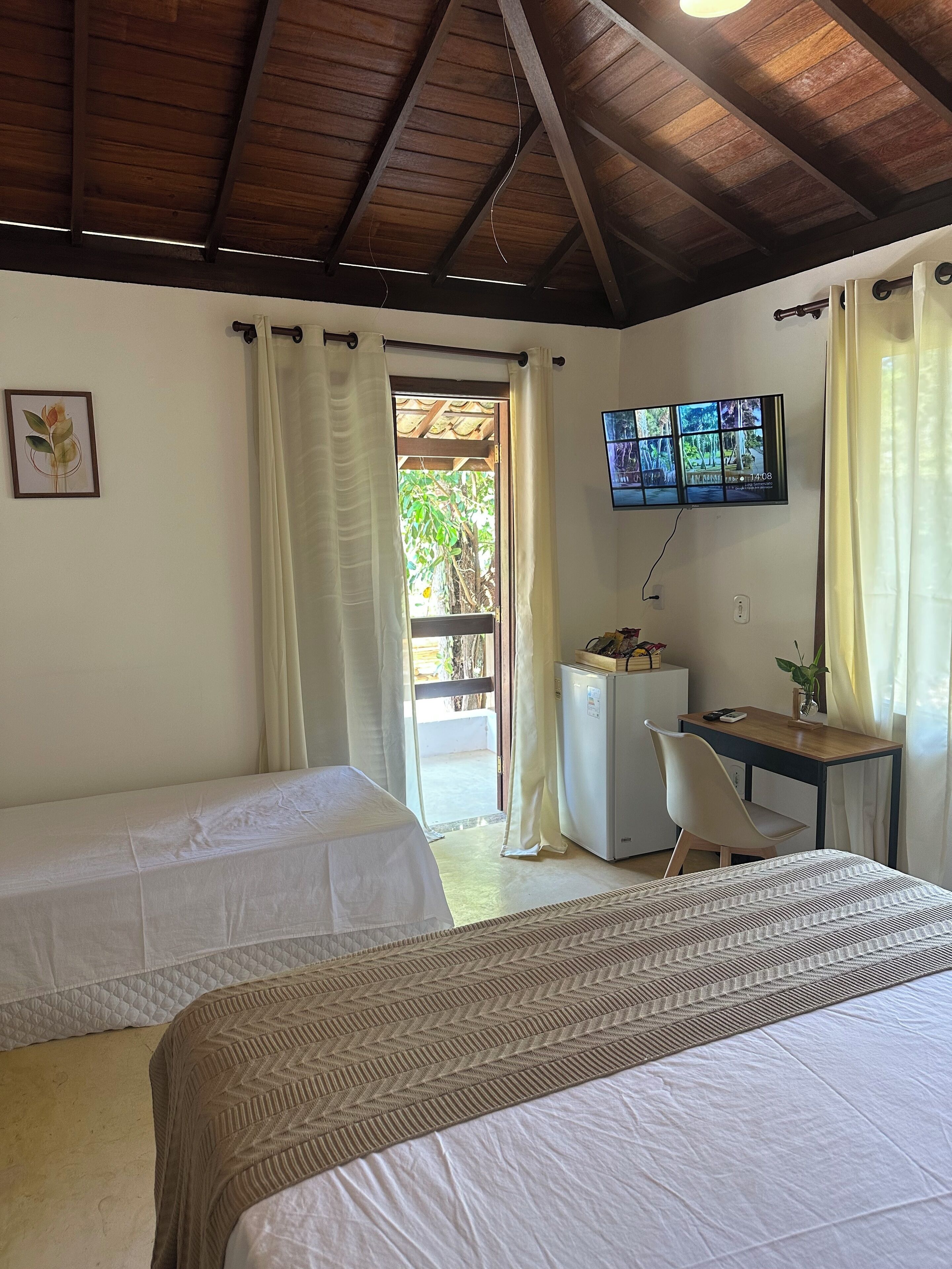 A room with two beds, a desk, a TV, and a view of the outdoors.