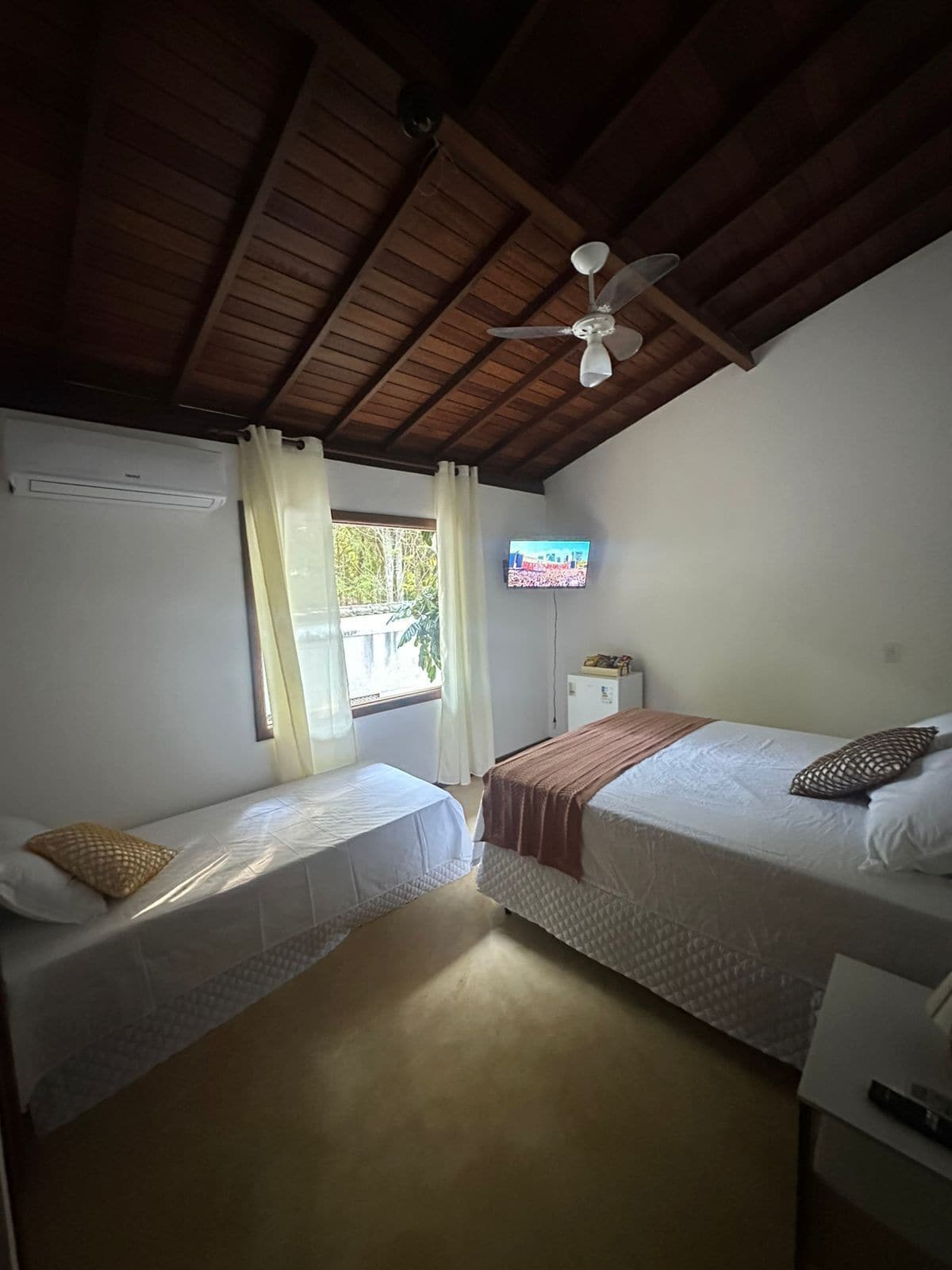 Een kamer met twee bedden, een plafondventilator, een televisie en een raam met gordijnen.