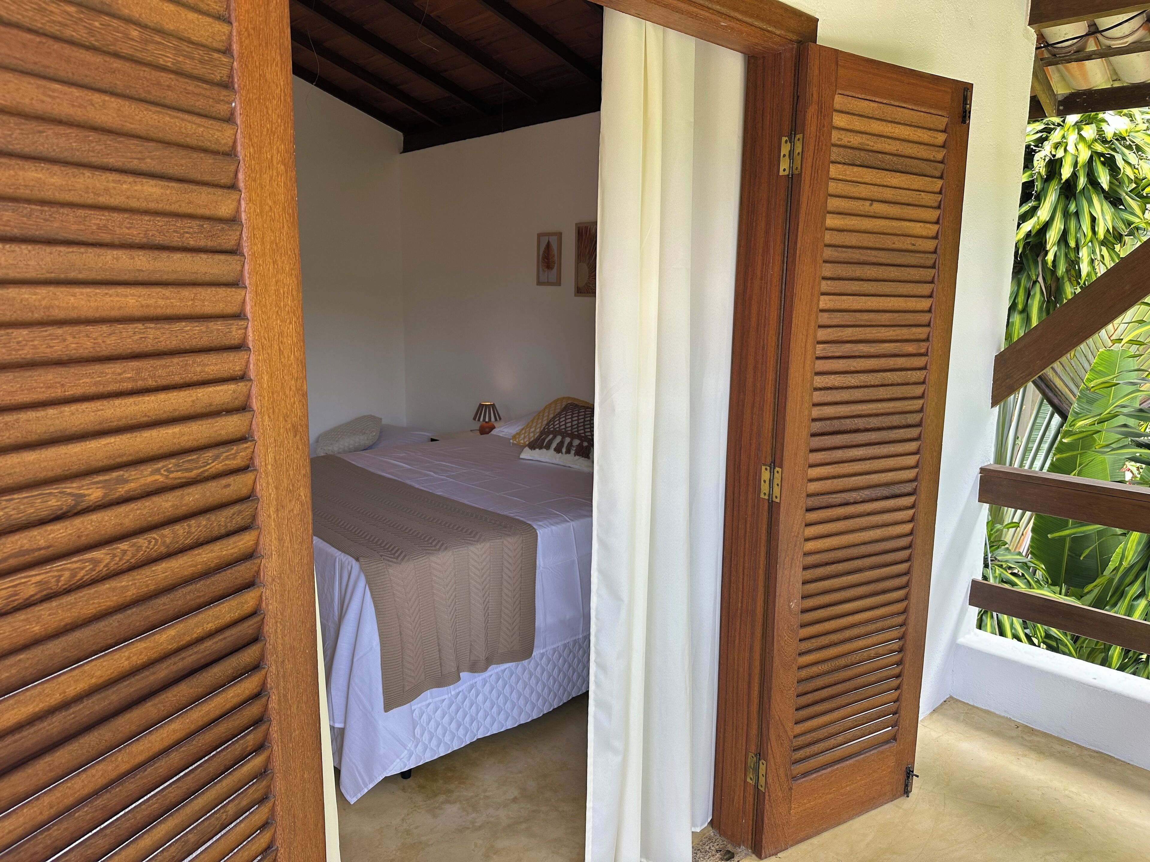 Un dormitorio con cama, mesita de noche y ventana con vistas a la vegetación.
